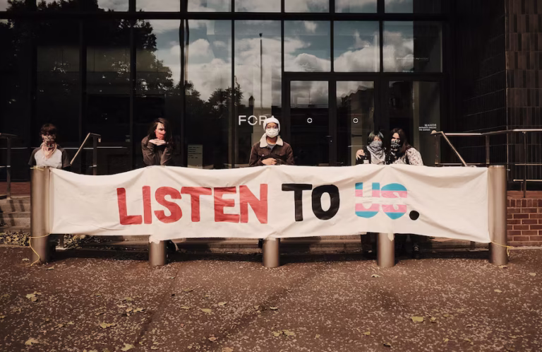 Protesters from Trans Kids Deserve Better outside the EHRC’s London office, with a banner reading 'LISTEN TO US.'